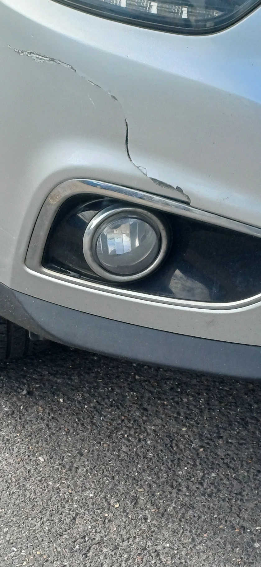 Cracked paint on a silver bumper near the fog light before repair